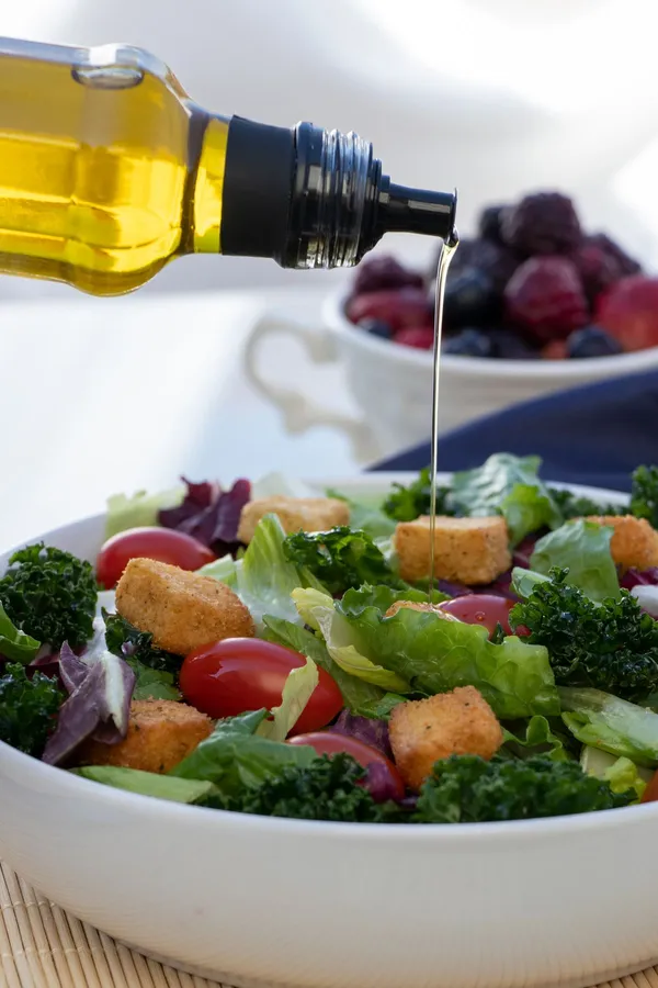 Golden olive oil being poured over a fresh salad